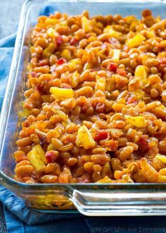 a glass casserole dish filled with baked beans and pineapples, on a blue cloth