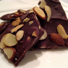 two pieces of chocolate with almonds on top sitting on a white plate next to each other