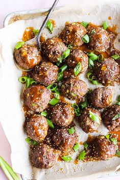 meatballs covered in sauce and green onions on a sheet of parchment paper with a spoon