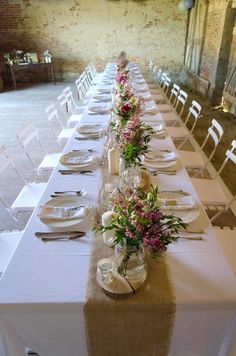 a long table is set with flowers and place settings for the guests to sit at