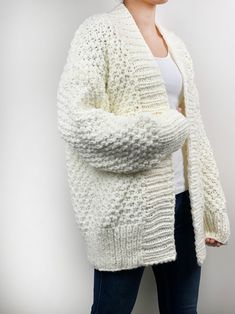 a woman wearing a white sweater and cardigan standing in front of a white wall