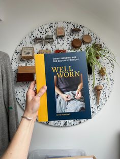 a person holding up a book in front of a wall decoration