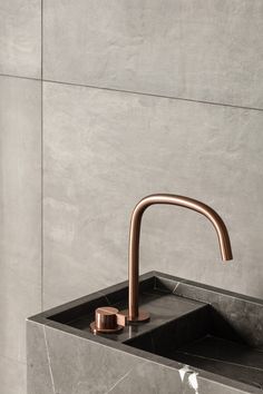 a bathroom sink with a copper faucet and marble counter top in front of a gray wall