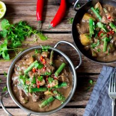 two bowls filled with meat and vegetables on top of a wooden table next to rice