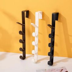 three black and white coat racks are next to each other on a yellow wall,