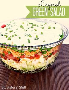 a large salad in a glass bowl on top of a wooden table with the words, layered green salad