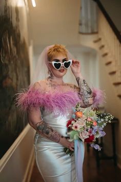 a woman in white dress holding a bouquet and wearing sunglasses with pink feathers on her head