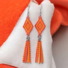 an orange and white beaded earrings with tassels hanging from it's sides