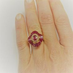 Here we have an exquisite vivid red ruby and diamond ballerina ring. The rubies here perfectly matched for color with astonishing intensity and clarity. The central ruby alone measures approximately 5.82mm x 3.80mm x 2.63mm weighing  0.65 carats. Additionally the ruby accents which are tapered baguettes weigh approximately 3.12 carats. These amazing accent rubies are arranged in a sensuous undulating circle surrounding the beautiful central red ruby. There are 13 points of VS/SI clarity G/H colo Luxury Red Ruby Ring Baguette Cut, Luxury Red Baguette Cut Ruby Ring, Red Diamond Baguette Cut Rings, Red Ruby Ring With Baguette Cut Center Stone, Red Baguette Cut Ruby Ring, Red Baguette Cut Lab-created Ruby Ring, Red 14k Gold Cluster Ring, Elegant Ruby Ring With Baguette Cut, Fine Jewelry Red Baguette Cut Ruby Ring