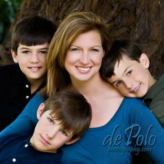 three boys and a woman are posing for a family photo in front of a tree