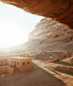 the sun shines through an opening in a rock formation with adobe buildings on it