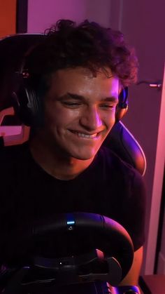 a young man wearing headphones sitting in front of a computer keyboard and smiling at the camera