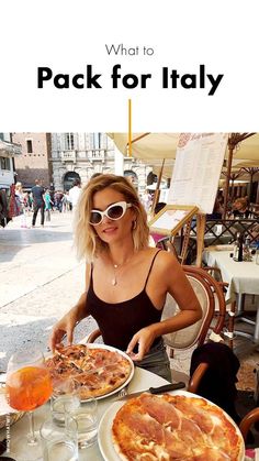 a woman sitting at a table with two pizzas and drinks in front of her