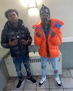 two young men standing next to each other in front of a bathroom mirror wearing jackets and jeans