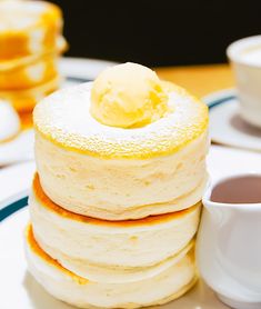 a stack of pancakes sitting on top of a table next to cups and saucers