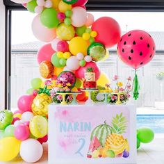 a table with balloons, watermelon and pineapples on it