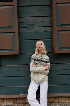 a woman standing in front of a blue building wearing white pants and a sweater with fair - fitting sleeves