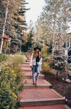 a woman walking up some steps in the woods wearing a cowboy hat and blue jeans