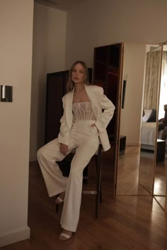 a woman sitting on top of a chair wearing white pants and a suit with an open front