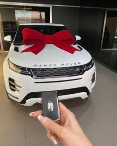 a person holding a cell phone in front of a white car with a red bow on it