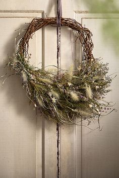 a wreath hanging on the front door of a house with dried grass and weeds in it