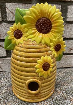 a yellow vase with sunflowers in it sitting on the ground next to a brick wall