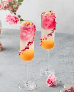 two glasses filled with drinks sitting on top of a table next to pink and yellow flowers