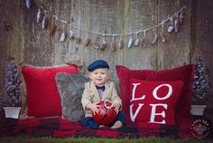 a young boy sitting on top of a red couch holding a heart shaped pillow with the word love written on it