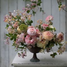 a vase filled with lots of pink flowers on top of a white table next to a wooden wall