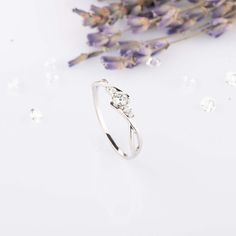 a diamond ring sitting on top of a white surface next to lavenders and flowers