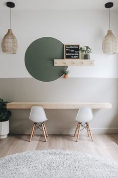 two white chairs sitting under a wooden table in front of a green circle on the wall