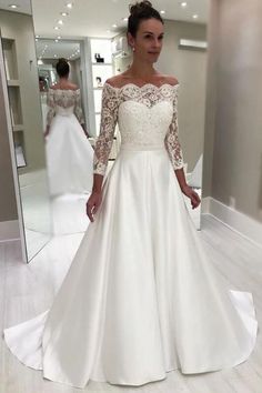 a woman in a white wedding dress looking at herself in the mirror with her hands on her hips