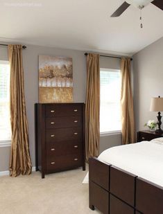 a bedroom with a bed, dresser and two windows covered in drapes on top of them