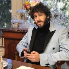 a man sitting at a table with a cell phone in his hand and looking off to the side