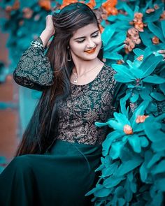 a woman with long black hair wearing a green dress and orange flowers in the background