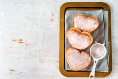 three heart shaped sugar cookies sitting on top of a wooden tray next to a spoon