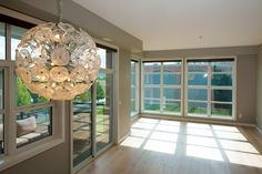 an empty living room with large windows and a chandelier hanging from the ceiling