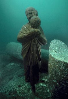 a man is standing in the water next to a large piece of stone and holding his head