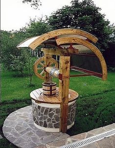 a wooden water pump sitting on top of a lush green field next to a stone walkway