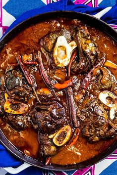 a pan filled with meat and vegetables on top of a blue table cloth next to a fork