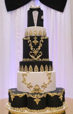 a three tiered cake with black and gold decorations on it's sides, topped with a tuxedo