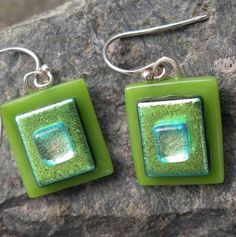 two green square shaped glass earrings sitting on top of a rocky surface with silver earwires