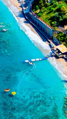 an aerial view of the ocean and beach with boats in it, near a bridge