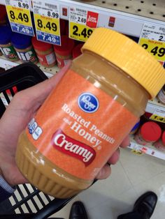 a person holding a jar of peanut butter in front of a store shelf with other items