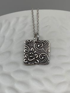 This minimalist tiny rose necklace has been entirely handmade using .999 fine silver. It has been cut out from fine silver precious metal clay, textured, fired and oxidized. The pendant hangs from a sterling silver diamond cut cable chain. This fine silver pendant features an embossed floral rose textured pattern on one side of the pendant and is reversible to a completely different embossed rose pattern on the reverse side. Pendant size: approximately 1/2 x 1/2 inches Chain length: adjustable a Unique Etched Sterling Silver Necklace, Etched Sterling Silver Necklaces, Artisan Silver Etched Necklace, Silver Etched Sterling Silver Necklace, Minimalist Etched Jewelry For Anniversary, Stamped Sterling Silver Necklaces, Stamped Silver Sterling Necklace, Sterling Silver Etched Necklace For Gift, Sterling Silver Stamped Necklaces