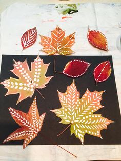 some leaves are laying on top of a piece of black paper and one is painted orange