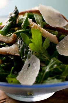 a salad with spinach, mushrooms and cheese in a blue bowl on a wooden table