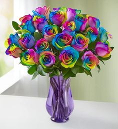 a purple vase filled with multi colored roses on top of a table next to a card