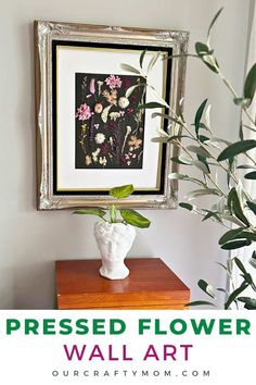 a white vase with flowers on top of a table next to a framed flower wall art