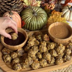 a person dipping something into a small bowl on top of a wooden tray next to pumpkins